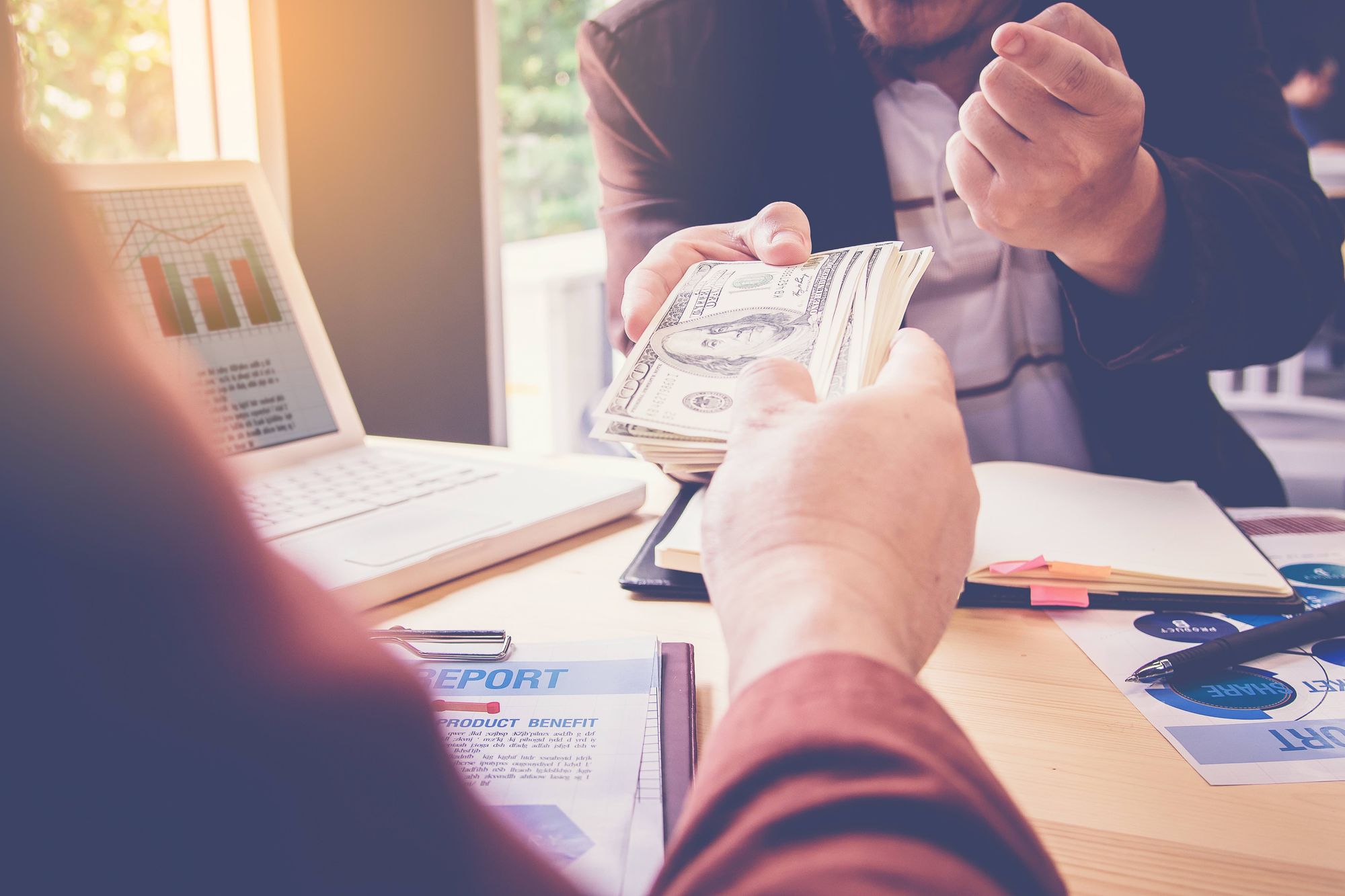 A lender handing a borrower a stack of hundred dollar bills.