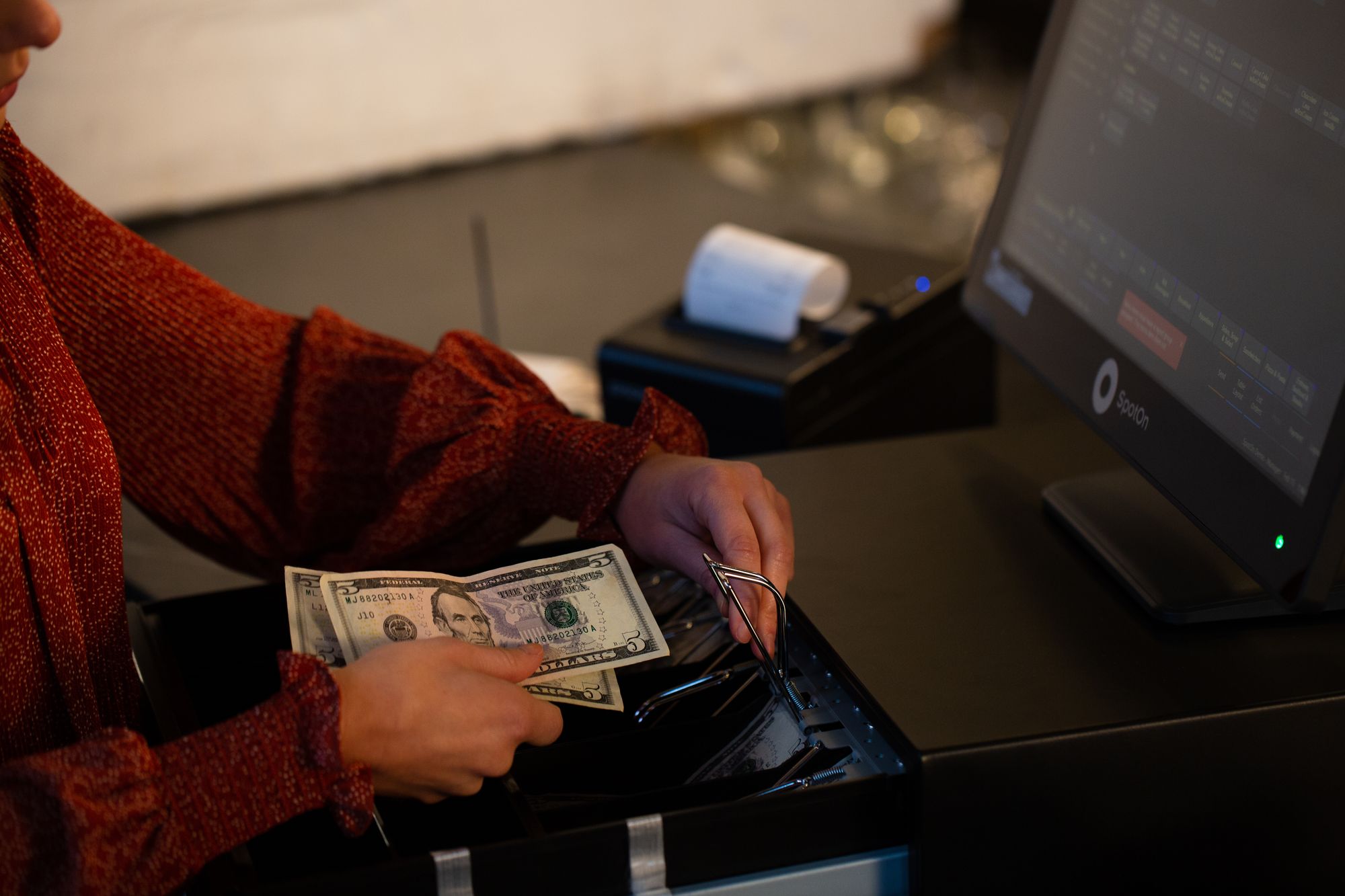Woman placing money in a cash drawer attached to SpotOn restaurant tech.