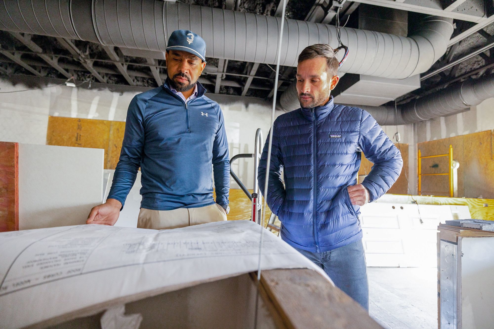 Two restaurant owners are looking at blueprints in an unfinished commercial space.