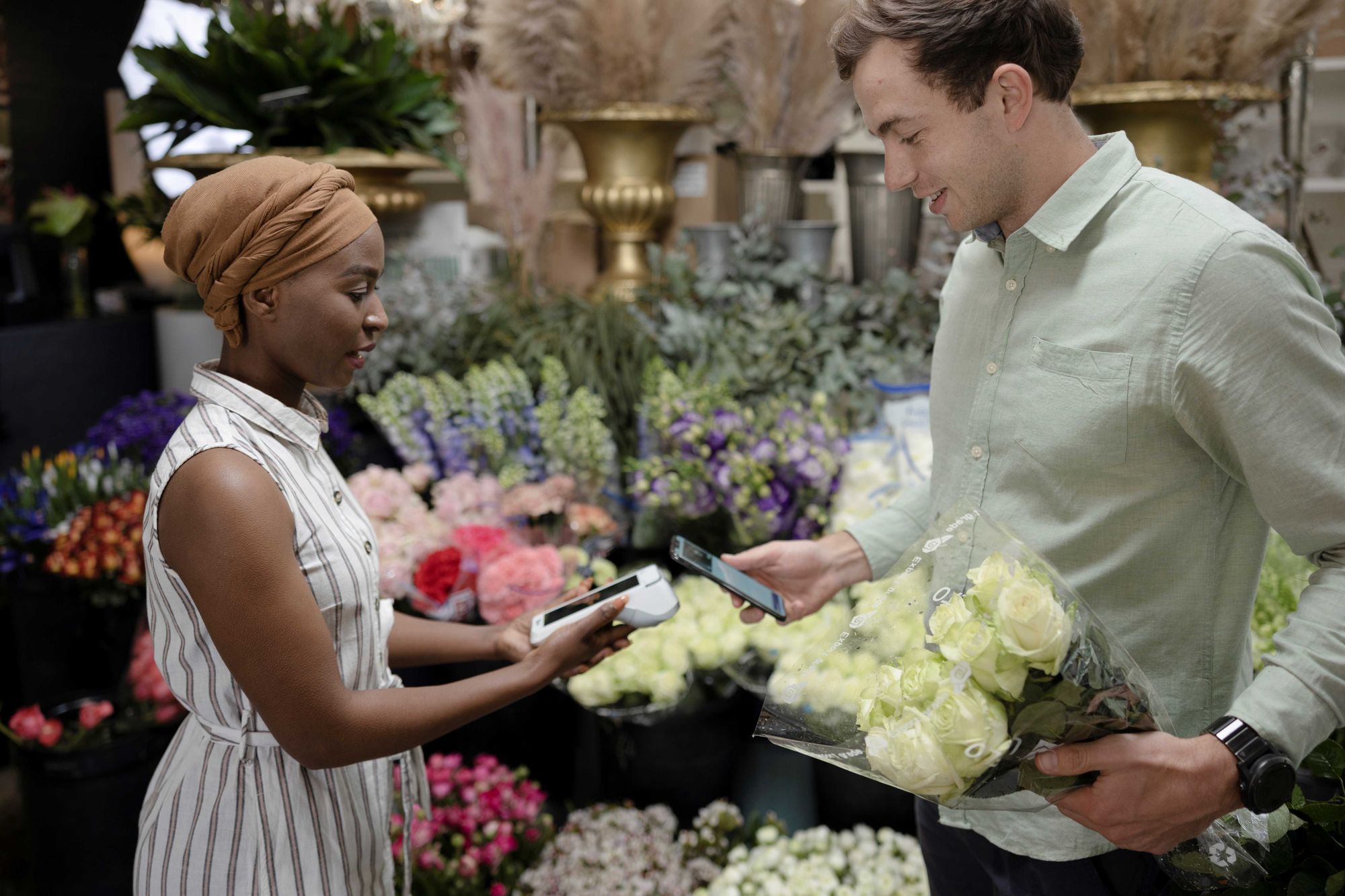 A customer taps his phone to pay on a handheld POS device at a floral shop