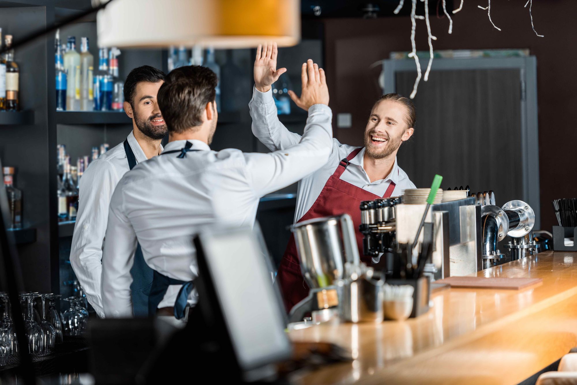 Three restaurant employees give high fives while standing behind a barista station.