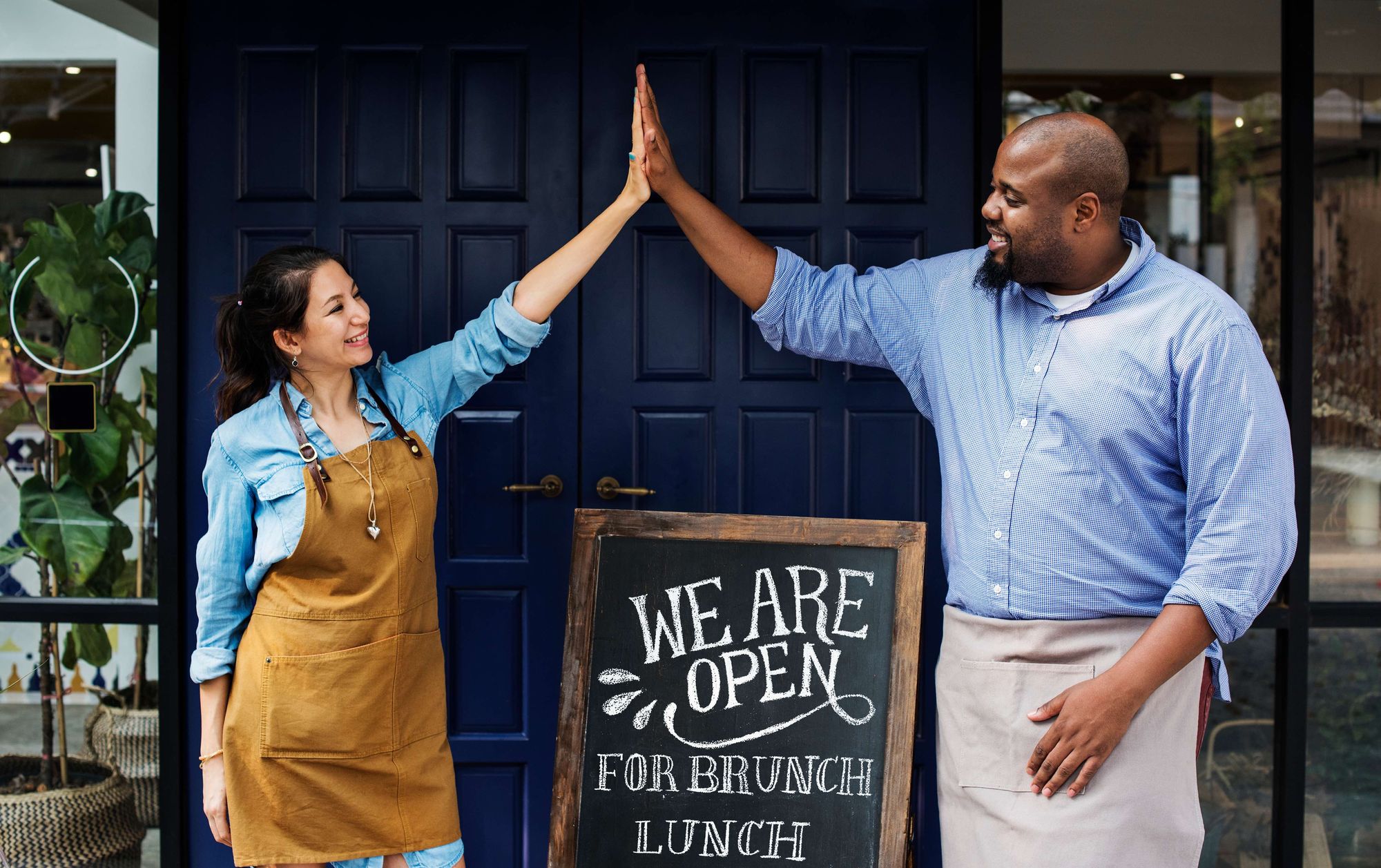Two employees give high fives in front of a sign that says "We are Open"