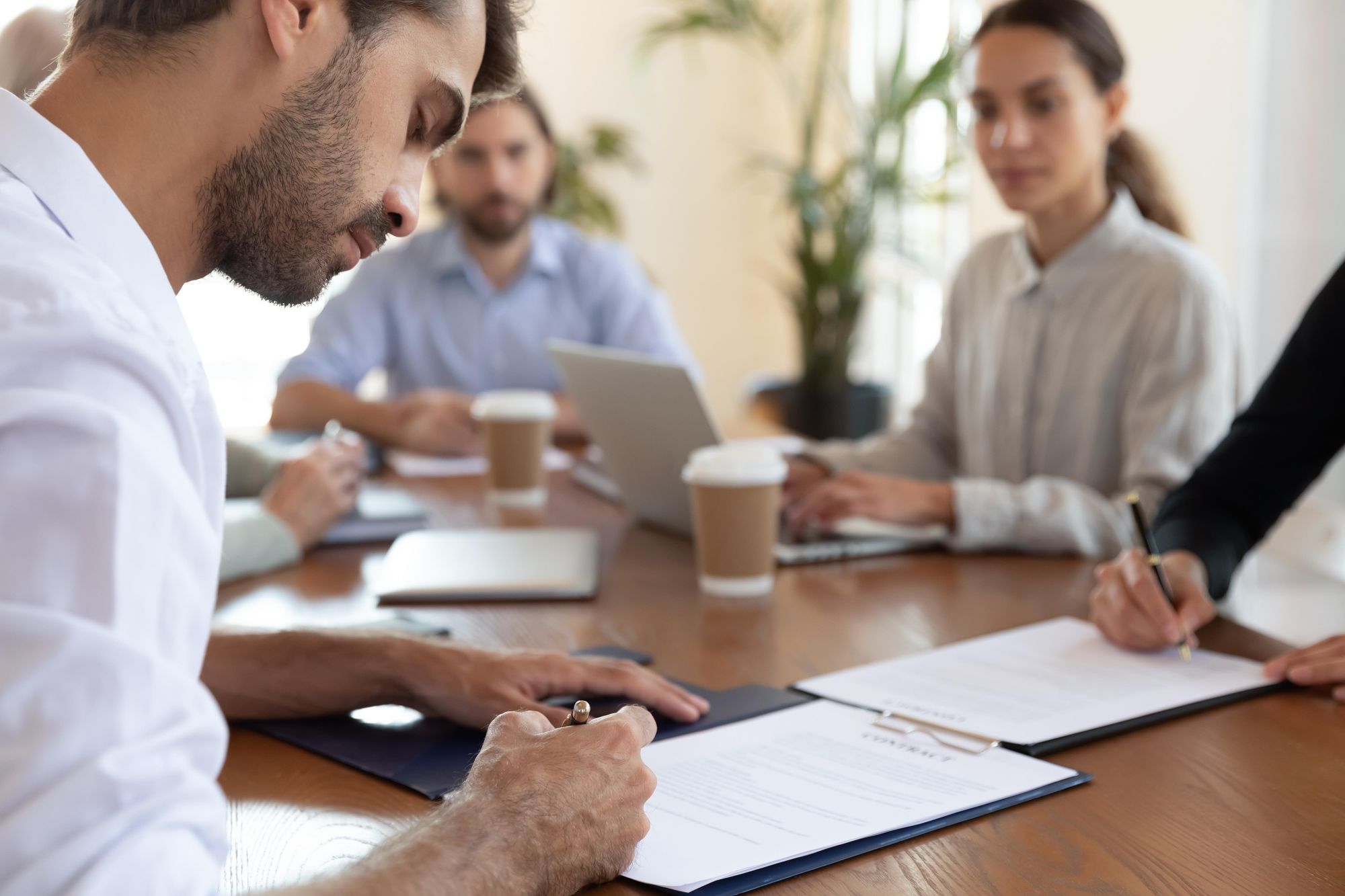 A man is signing papers while sitting at a table with legal professionals.