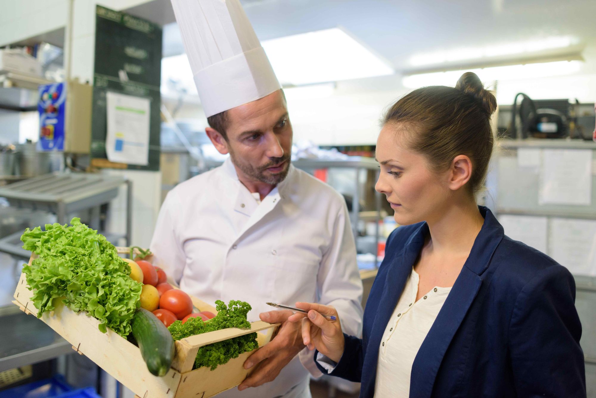 A restaurant manager inspects a box of produce that the chef is holding.