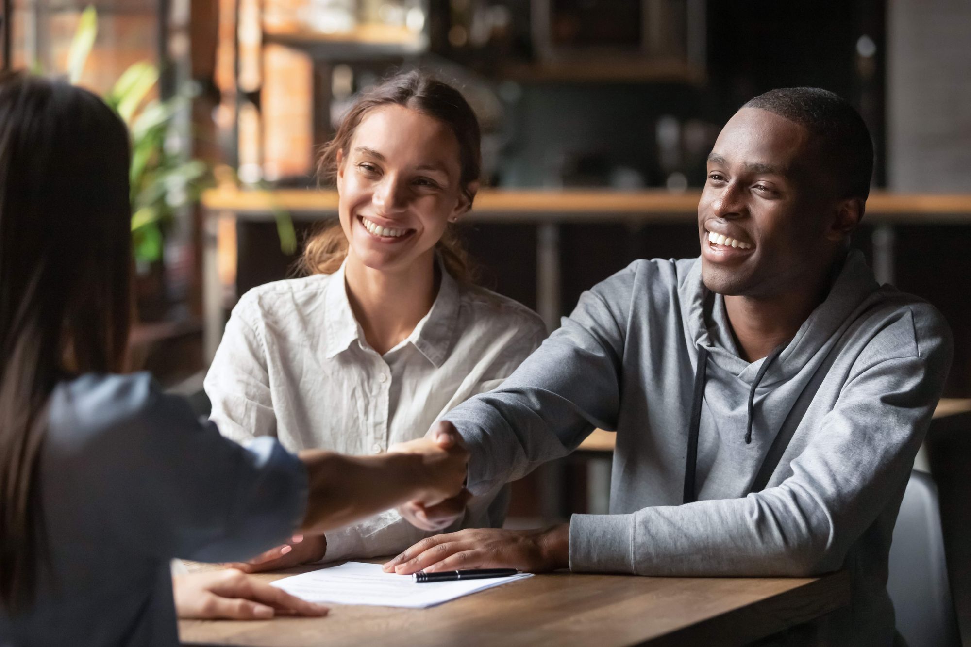 A man and woman are sitting across from a business lender, and the man is shaking her hand.