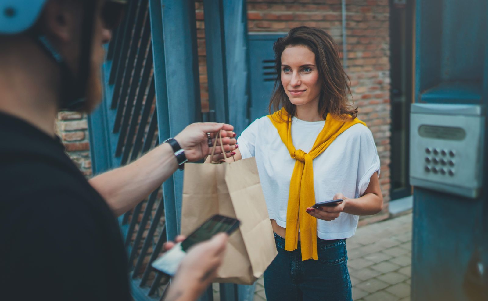 A delivery couriers hands a customer a bag with their restaurant food order.