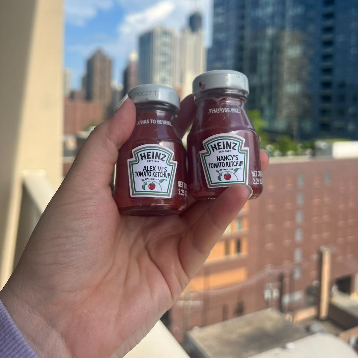 A hand holds two small Heinz ketchup bottles