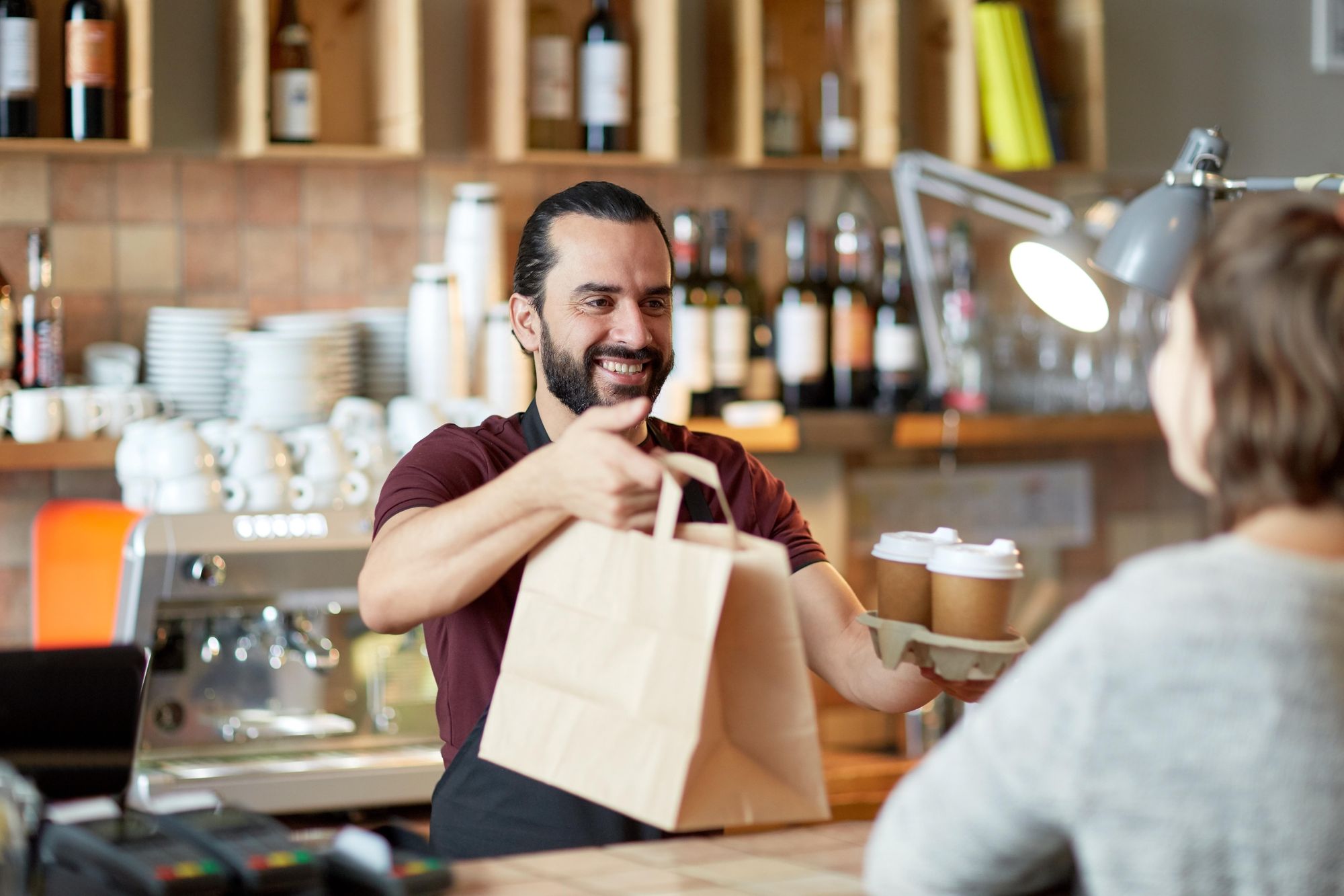 A restaurant worker hands a takeout order to a customer at the counter.