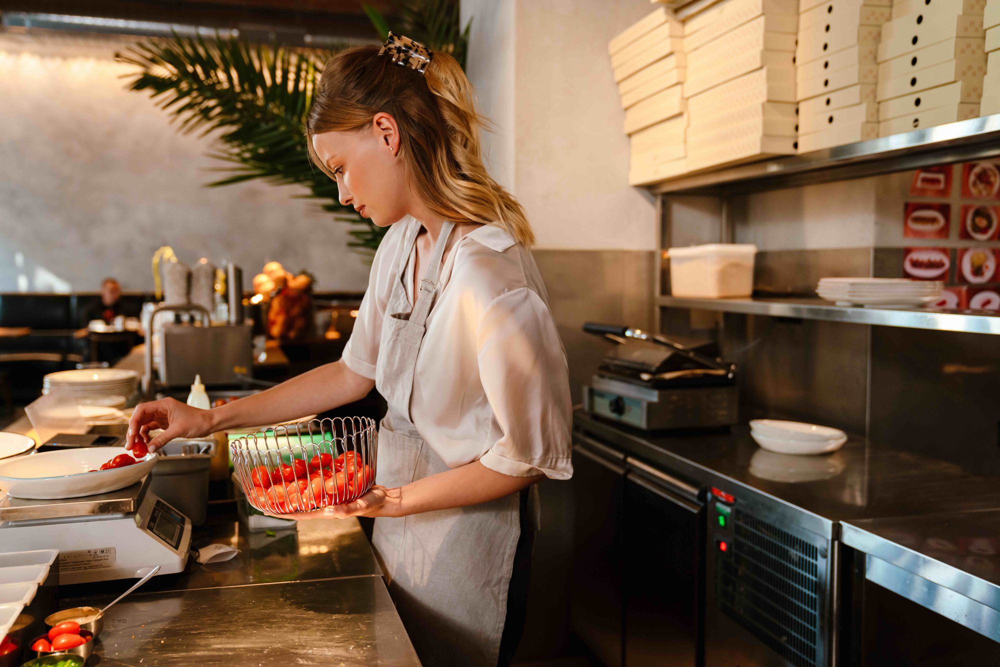 A food worker in a kitchen weighing cherry tomatoes.