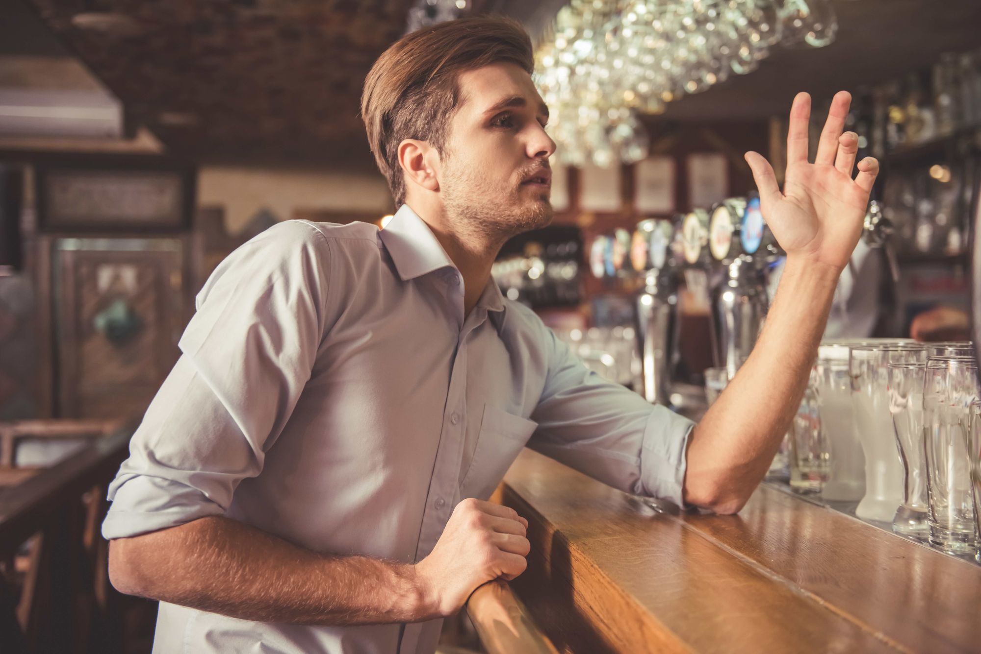 A man at a bar raises his hand to order a drink.