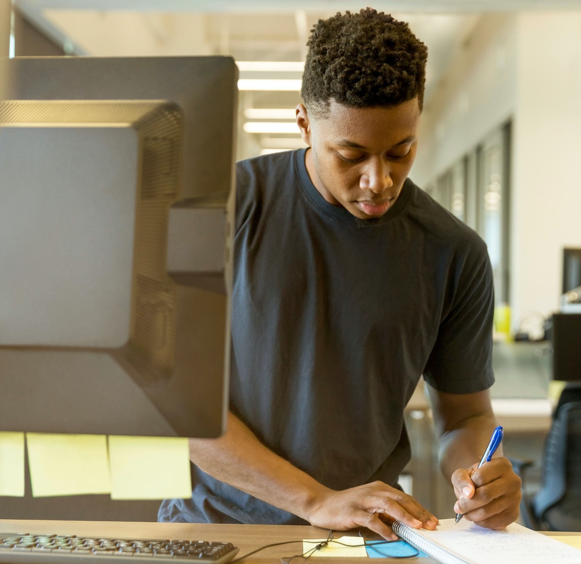 A young man taking notes and applying for a job in front of a computer.