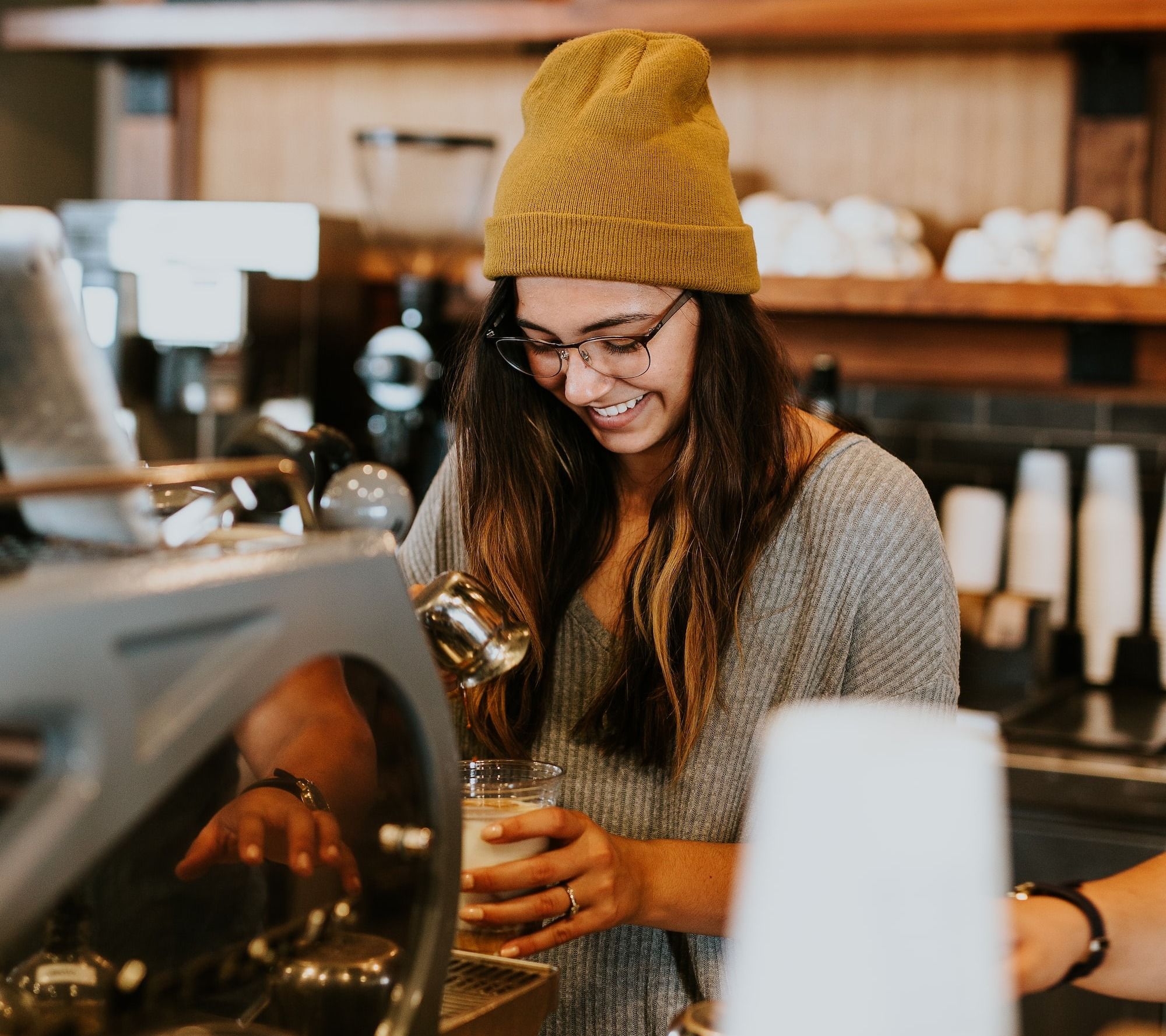 Barista smiling and pouring coffee at a coffee shop.