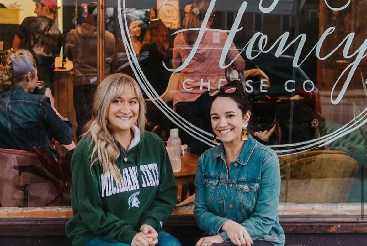 Two women business owners smile in front of a charcuterie business.