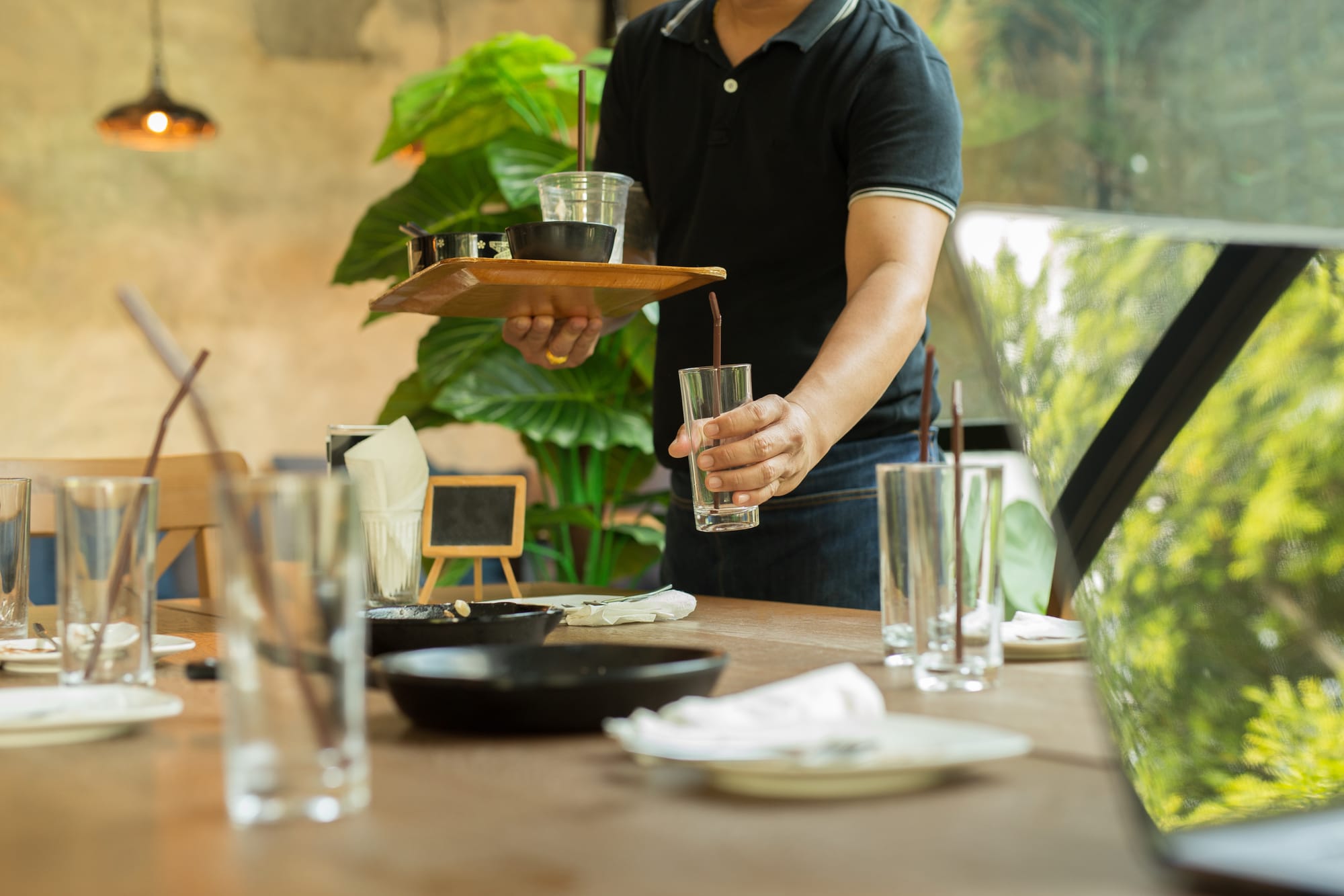 A busser is holding a tray while clearing a glass from a table.