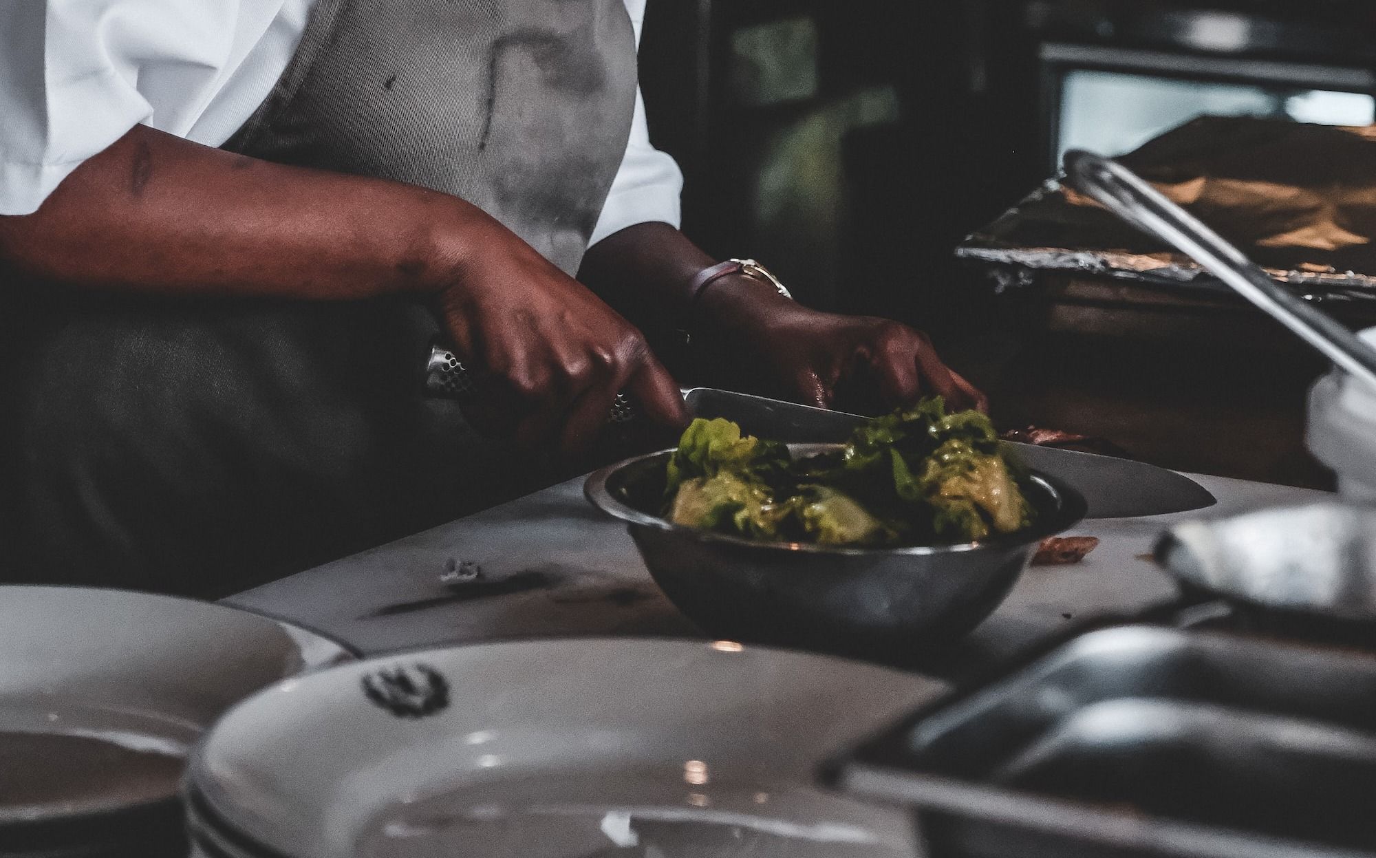 Chef in back kitchen using a knife to prep meals for guests ordering at a point-of-sale.