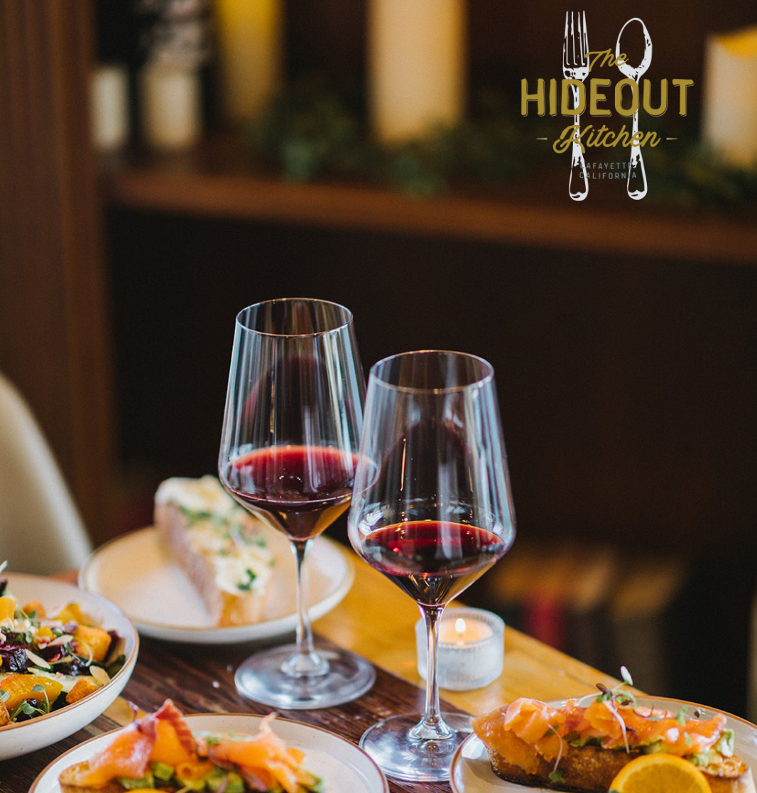 A table at the Hideout Kitchen with dinner and 2 wine glasses.