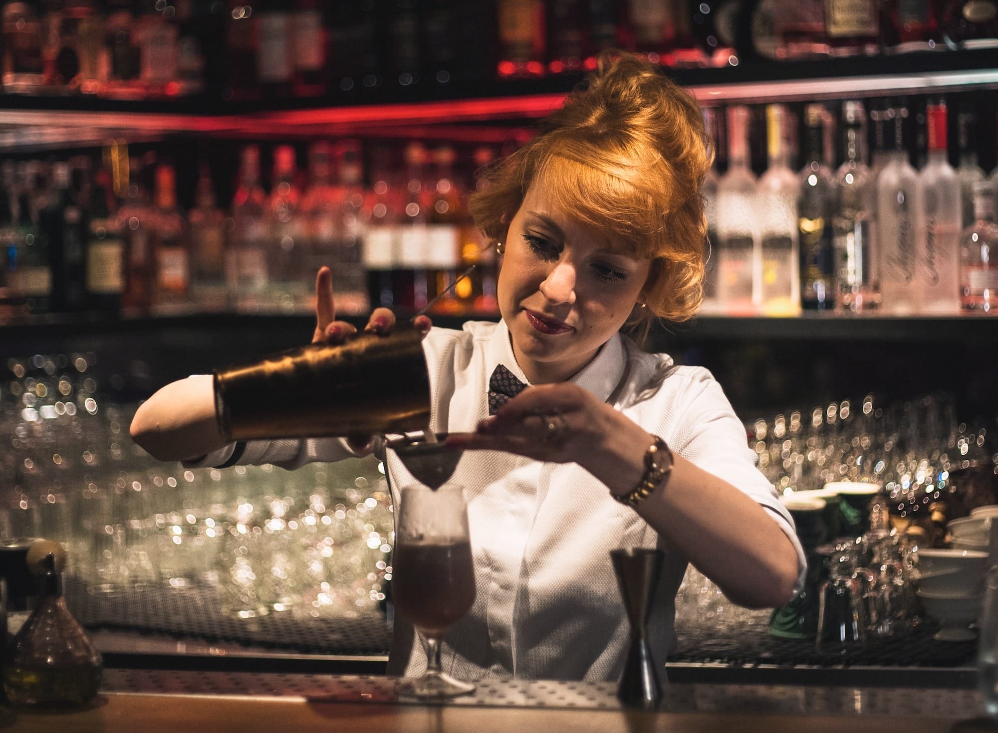 woman pouring bar shaker in clear glass stem glass on bar counter