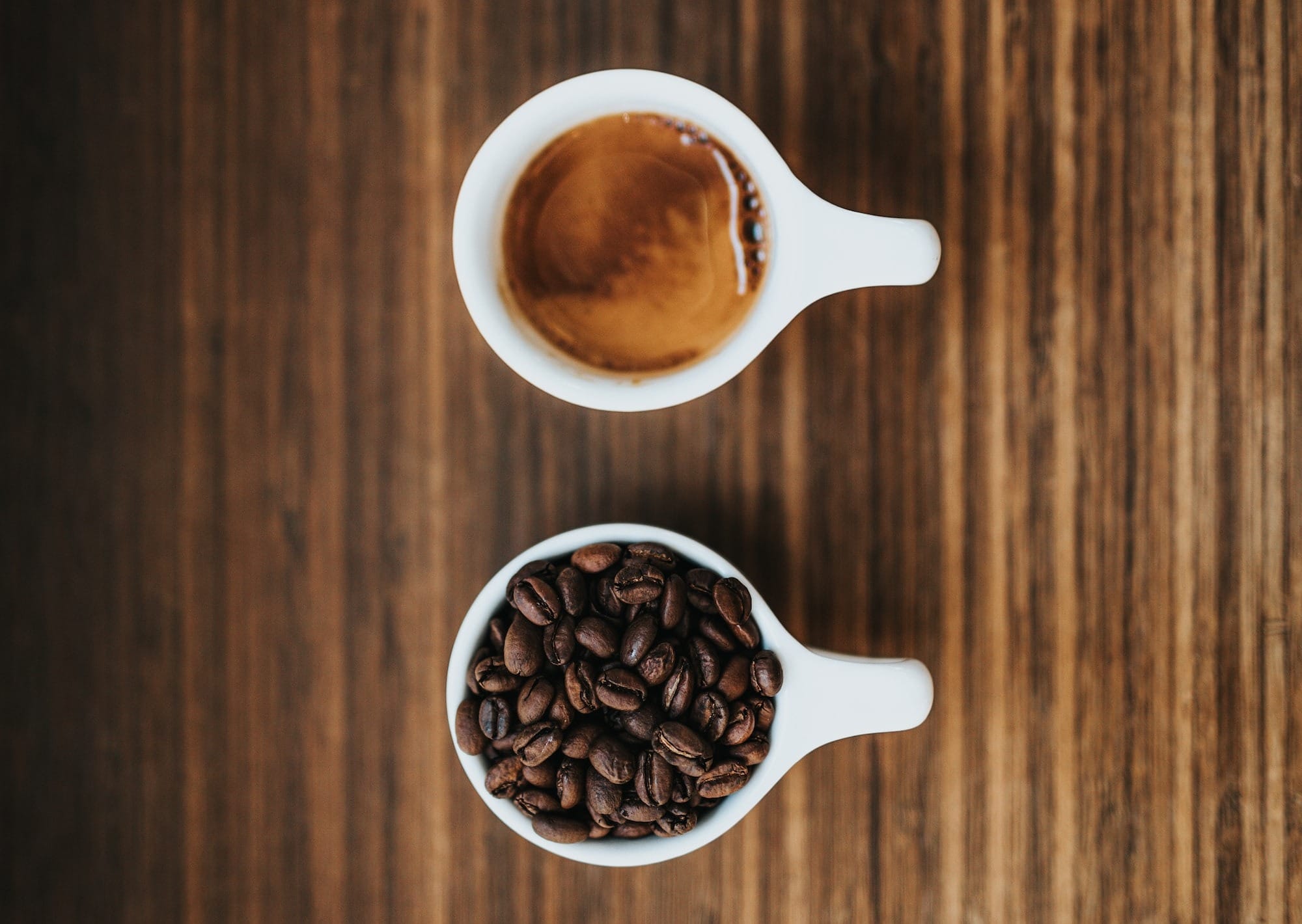 Two white ceramic mugs one of coffee beans and the other an espresso.