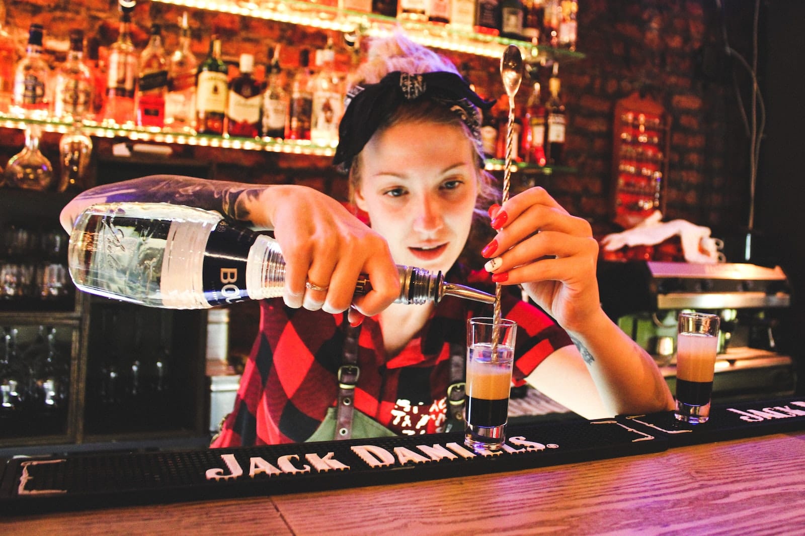 Bartender pouring a well drink into a highball glass.