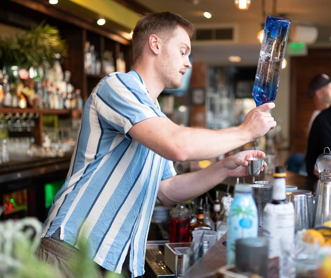 Bartender pouring a well drink in a bar with vodka.