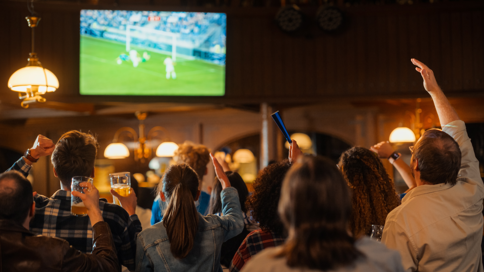 A crowd at a bar watches a soccer match on TV.