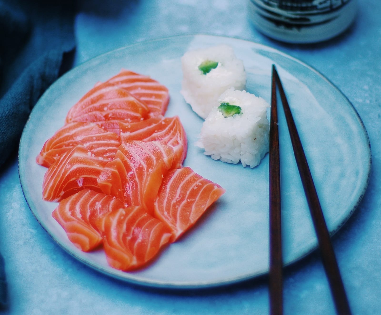 Sashimi sushi and balls of rice on a plate next to chopsticks.