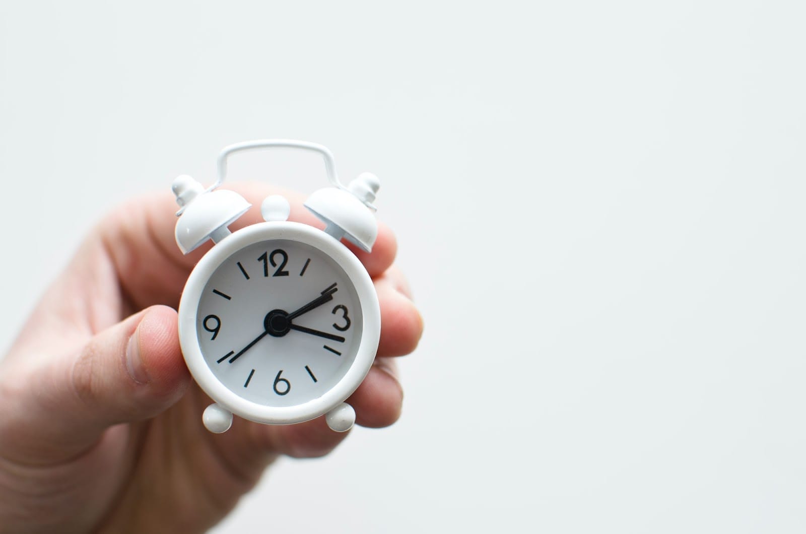 Tiny white alarm clock held in someone's hands like a calming bird.