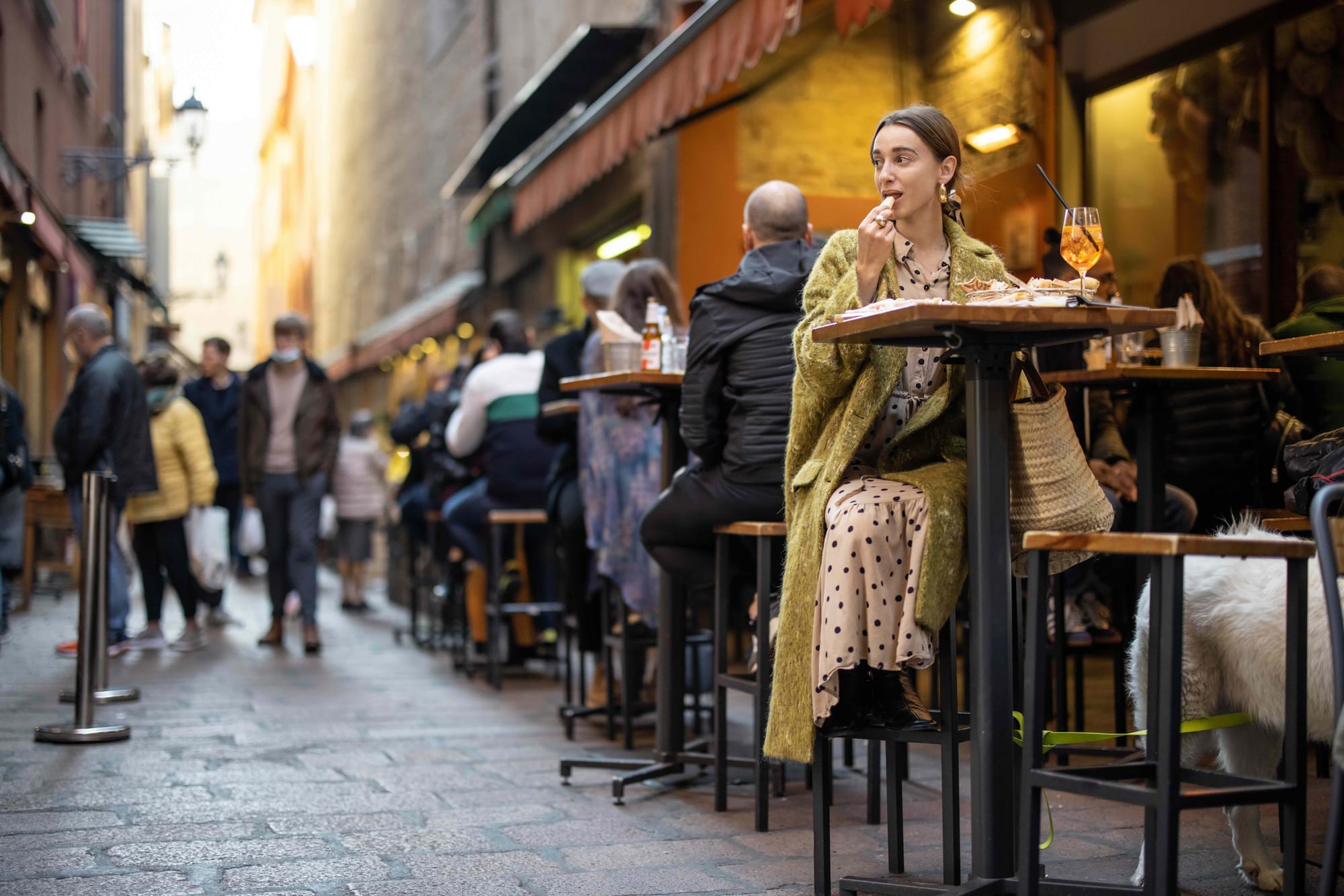 People eat at outside tables at restaurants on narrow road.