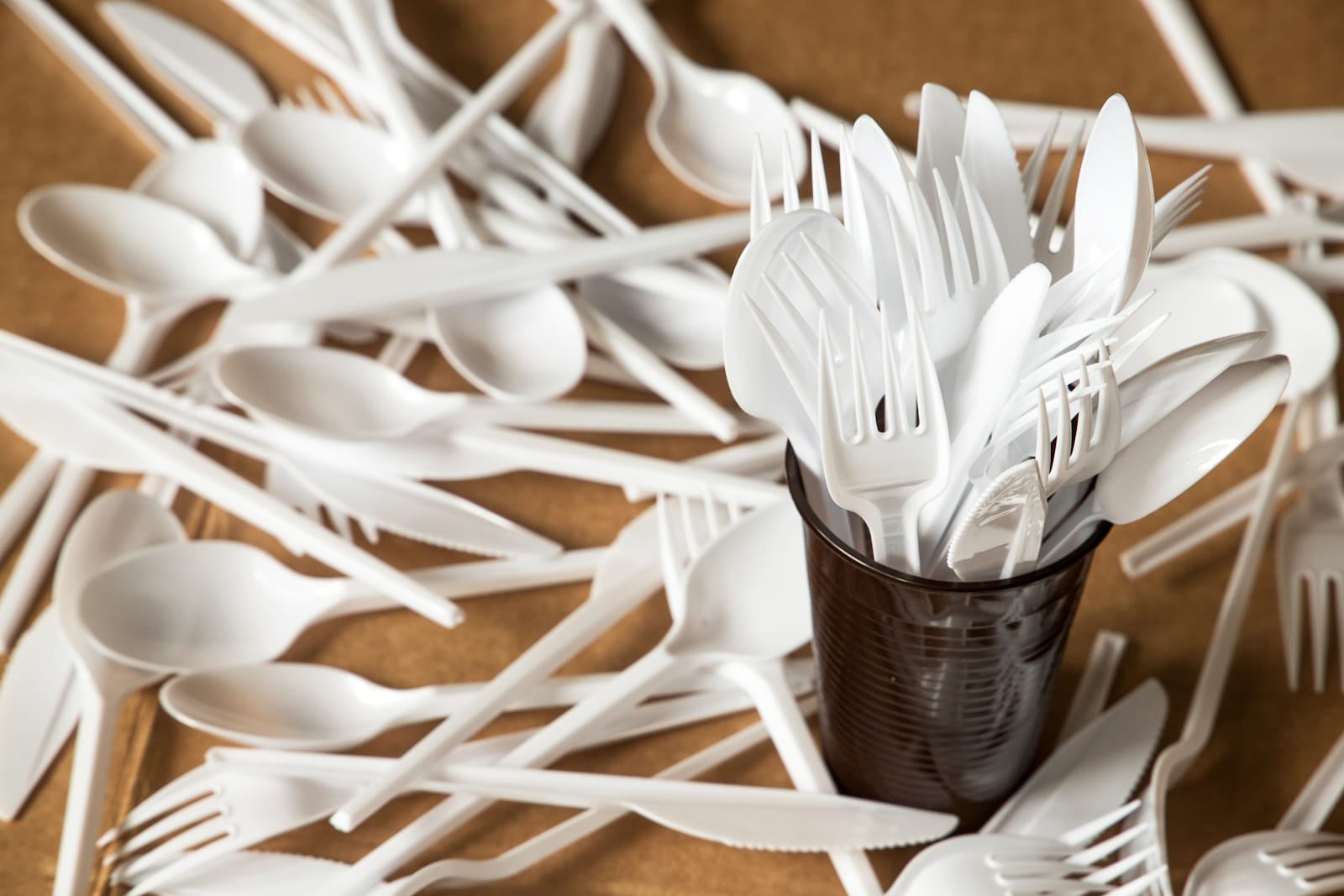 Plastic forks, spoons, and knives are in a cup and spread out on a table.