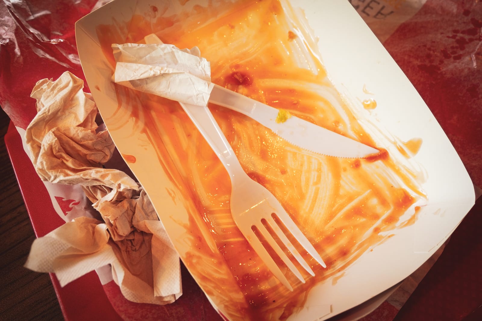 Used plastic utensils, paper napkins, and food tray sit on a table.