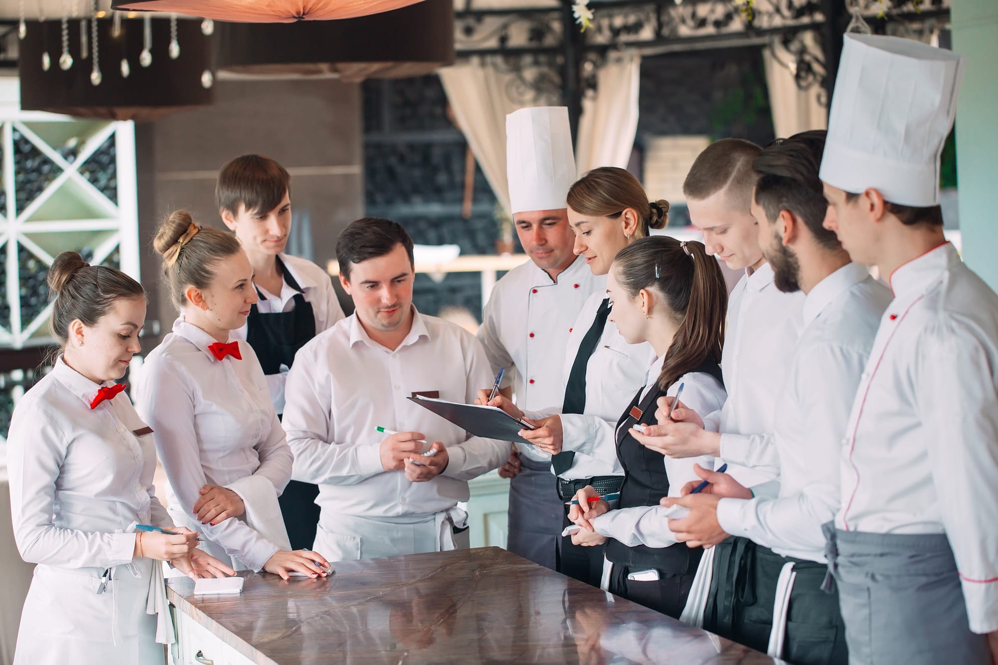 A group of restaurant severs and chefs standing around a manager.