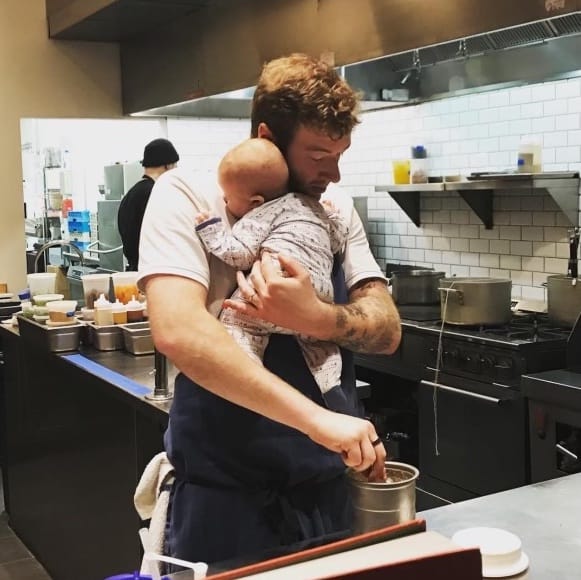 Davey Rabinowitz prepares food while holding a baby.