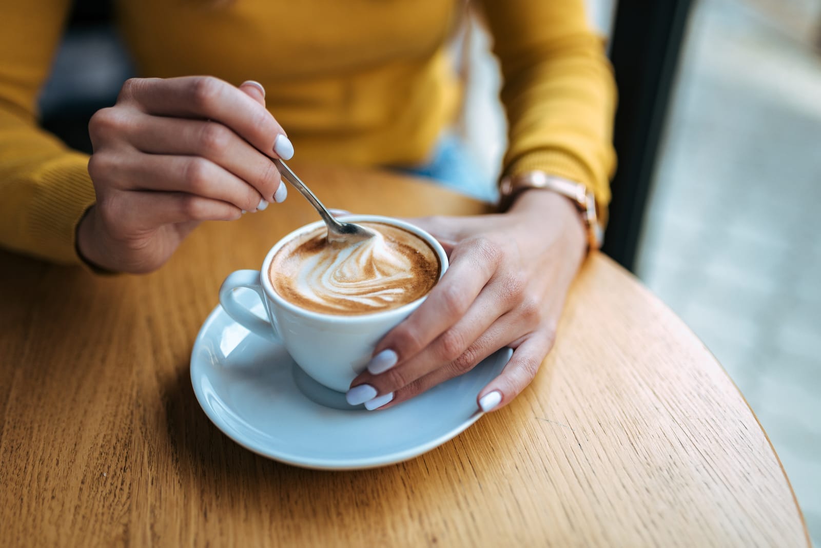 Woman at coffee shop mixing latte and latte milk foam with teaspoon.