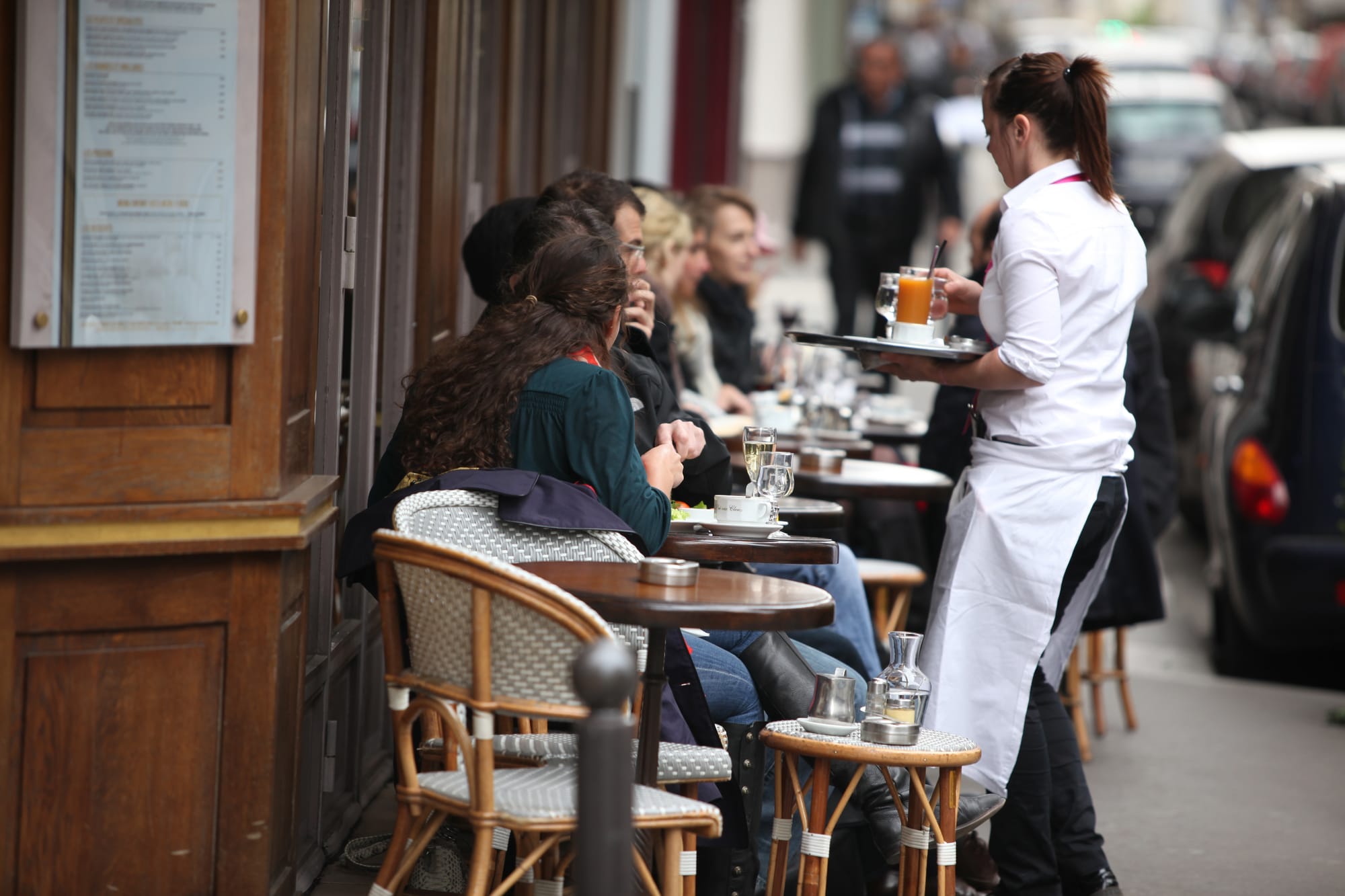 Eurpoean cafe patron guests in a bistro outdoor seating area with cafe coffee waitress server.