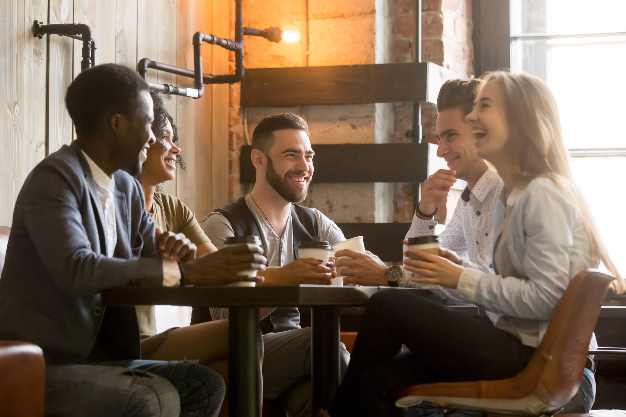 Many patrons in a coffee shop laughing and sipping on coffee and tea beverages.