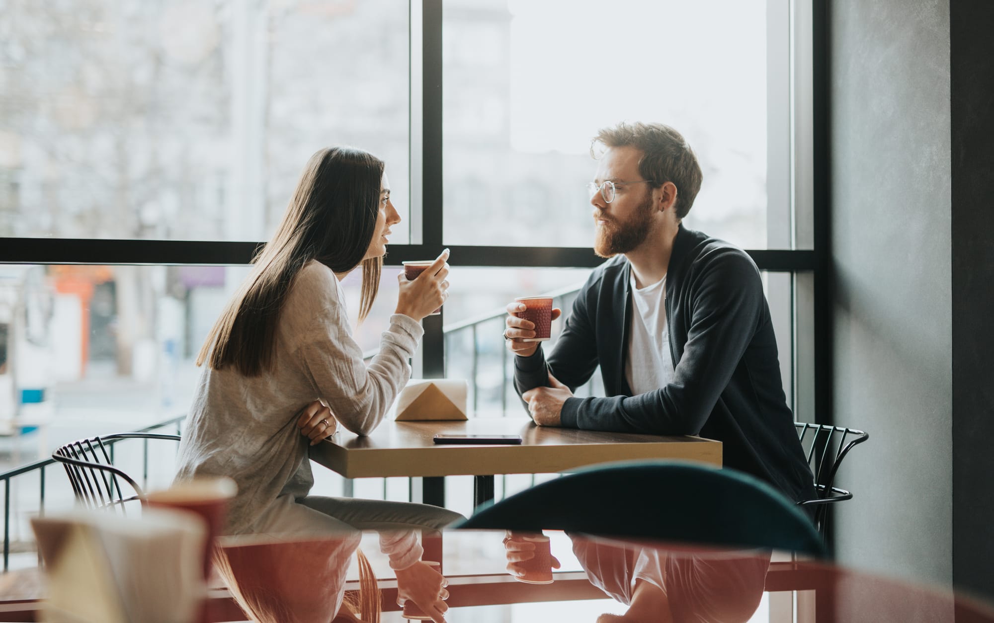 Two people at a coffee shop talk and sip coffee about a plethora of topics.