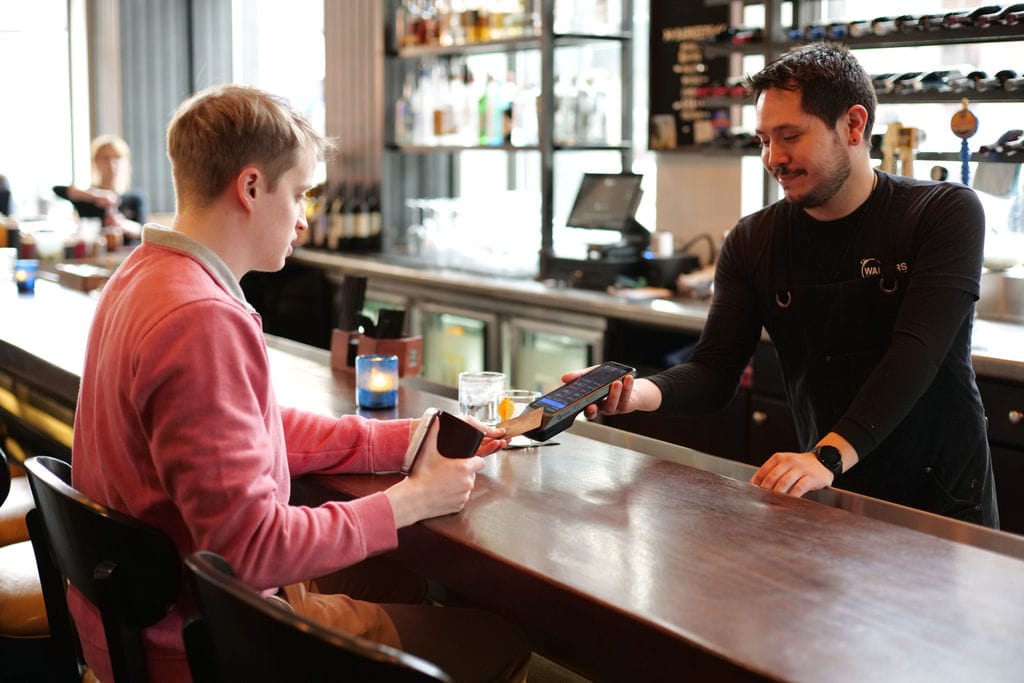 Guest tips with handheld pos system at a bar.