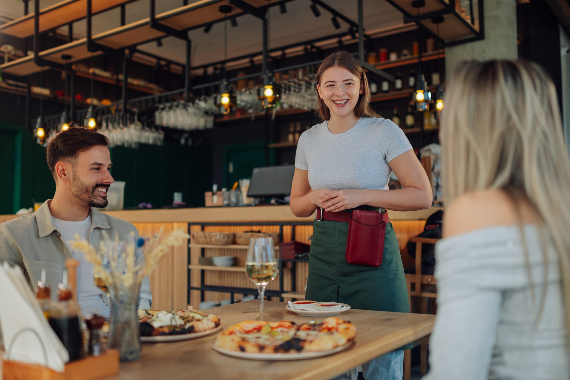 Server talking with guests with pizza and wine on the table.