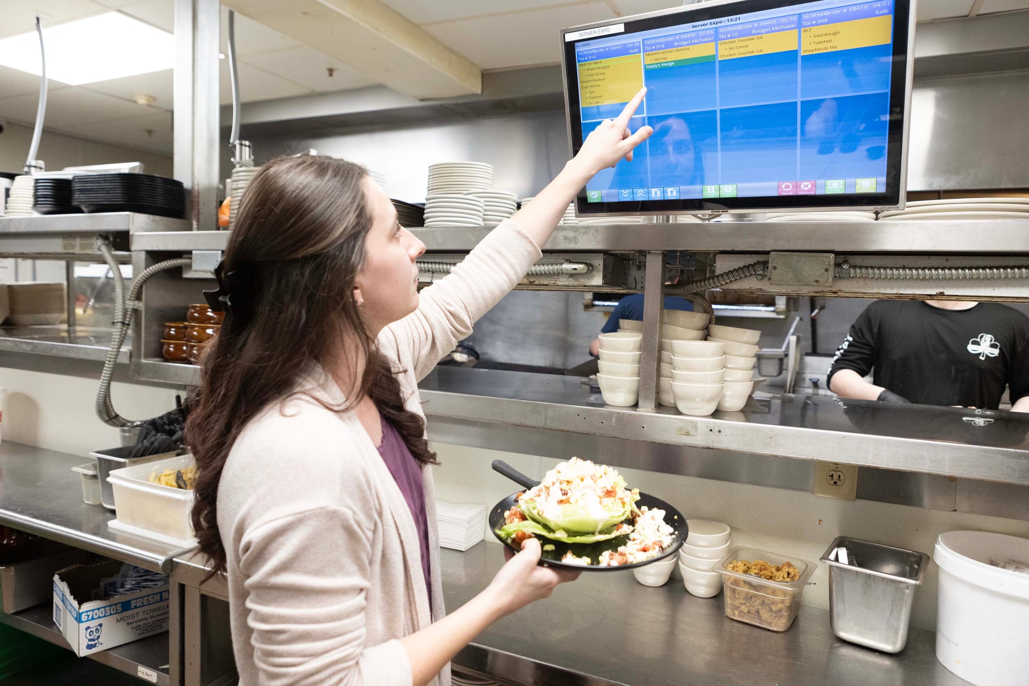 A restaurant worker advances an order on a KDS screen