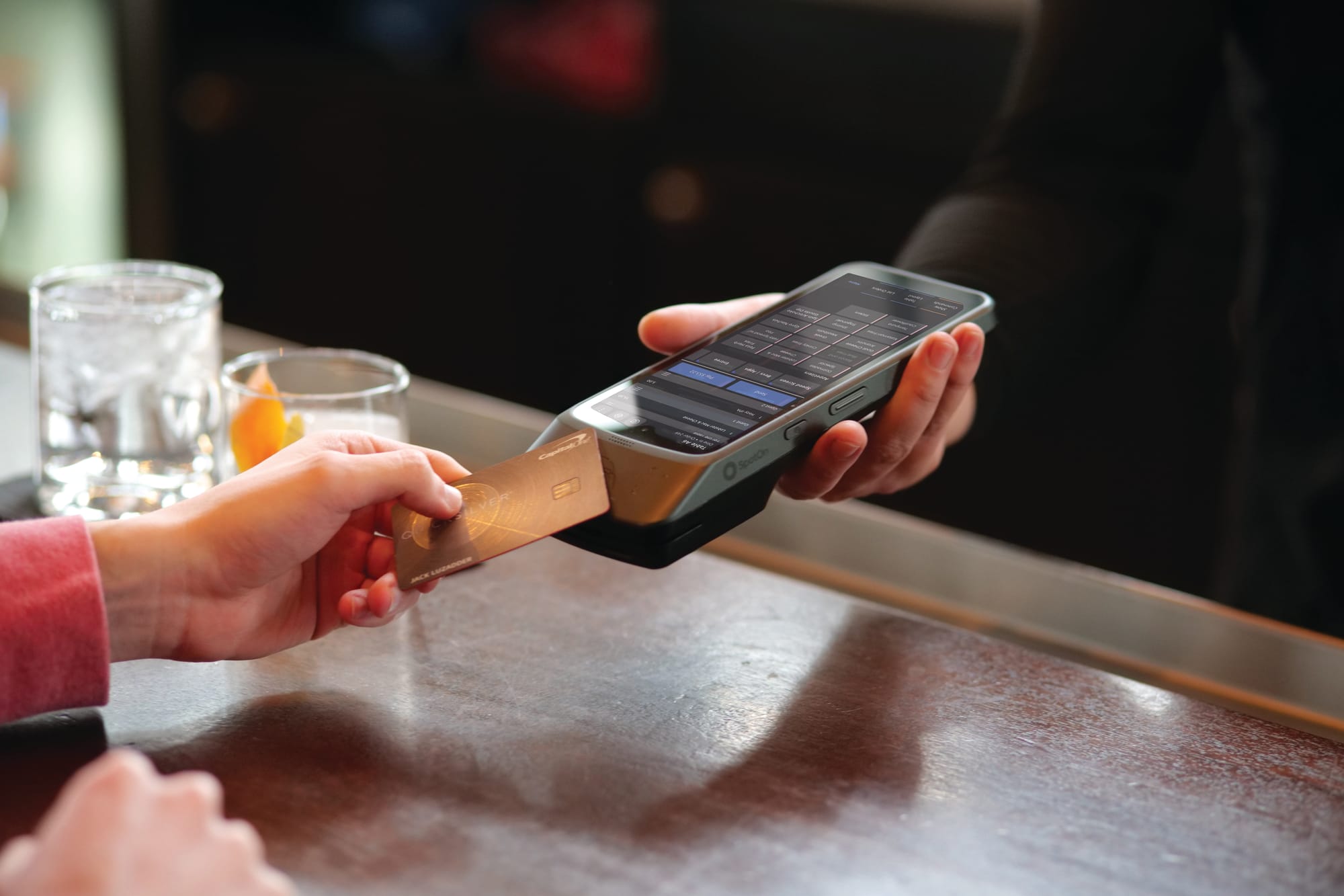 A server holds out a handheld restaurant POS for a guest to pay with their card