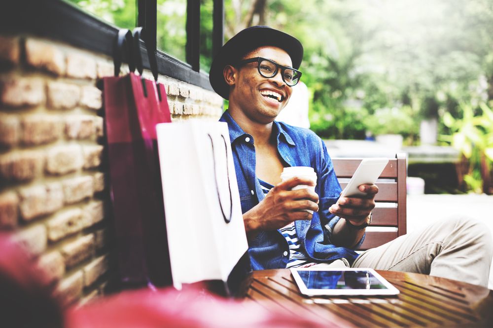 Man with glasses holding a coffee and phone at a cafe.