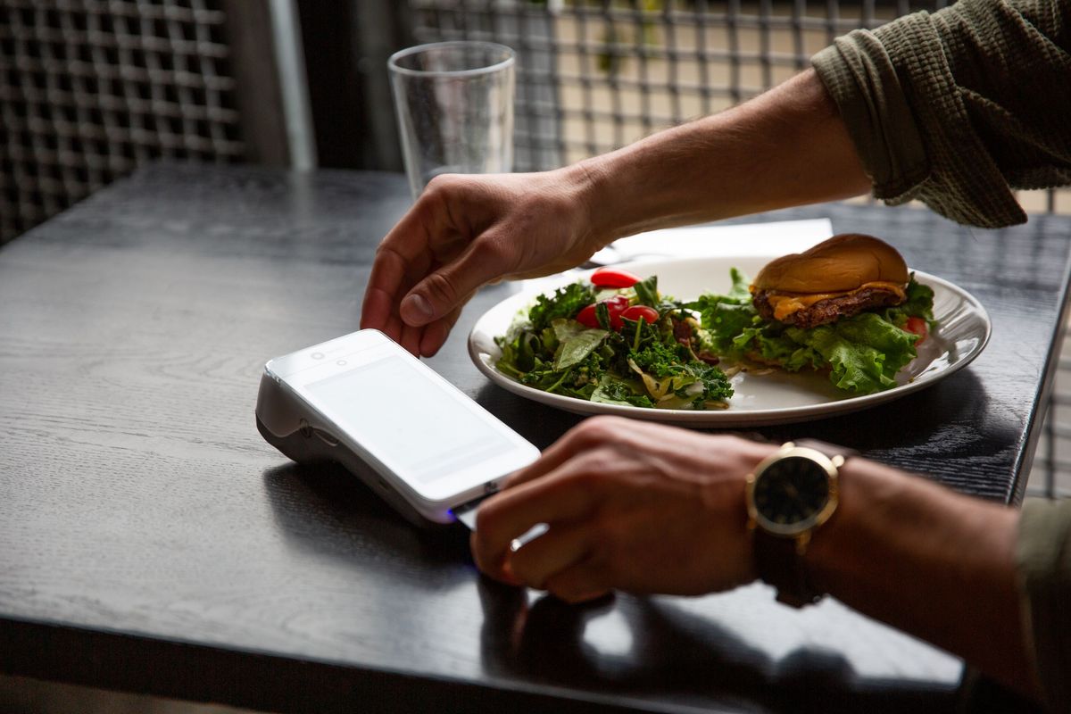 A restaurant guest pays their bill using a SpotOn Serve handheld POS device.