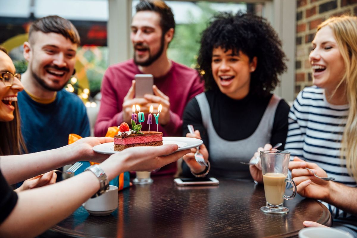 Guests at a restaurant hold up a birthday cake with candles and sing happy birthday 