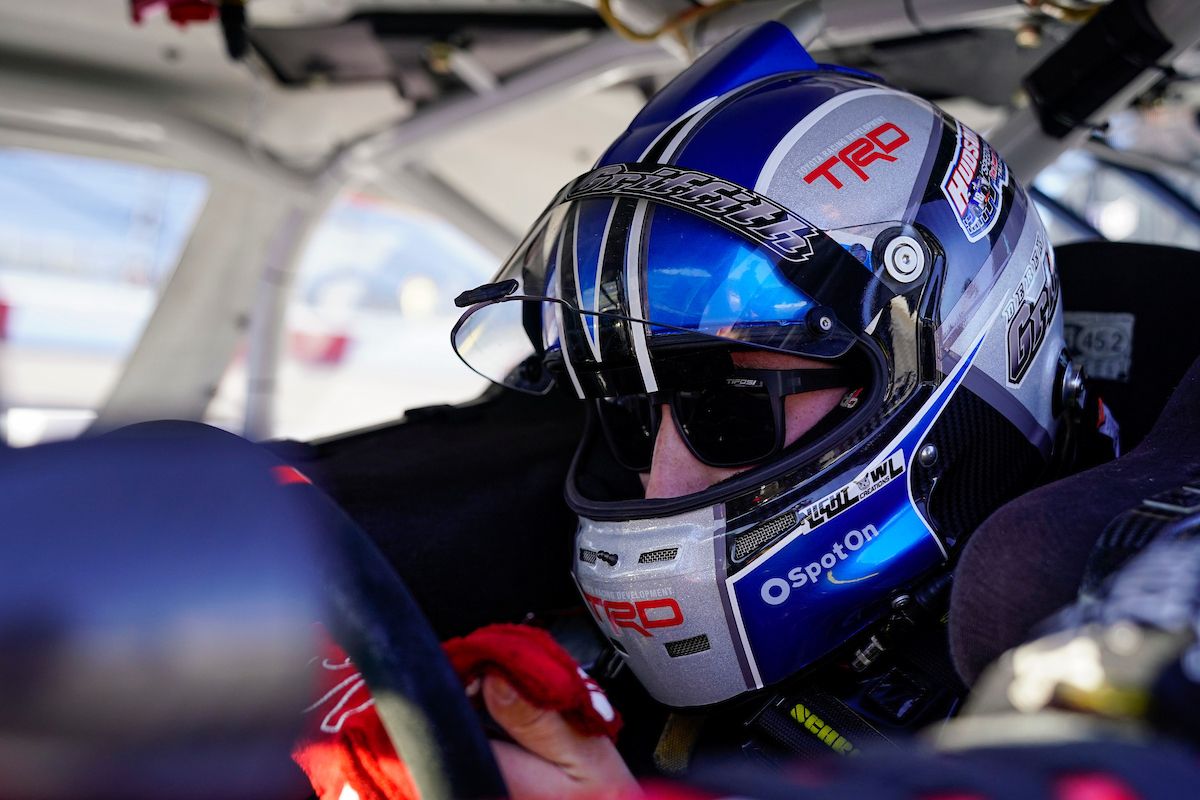 Man wearing a blue race helmet is sitting inside a race car.