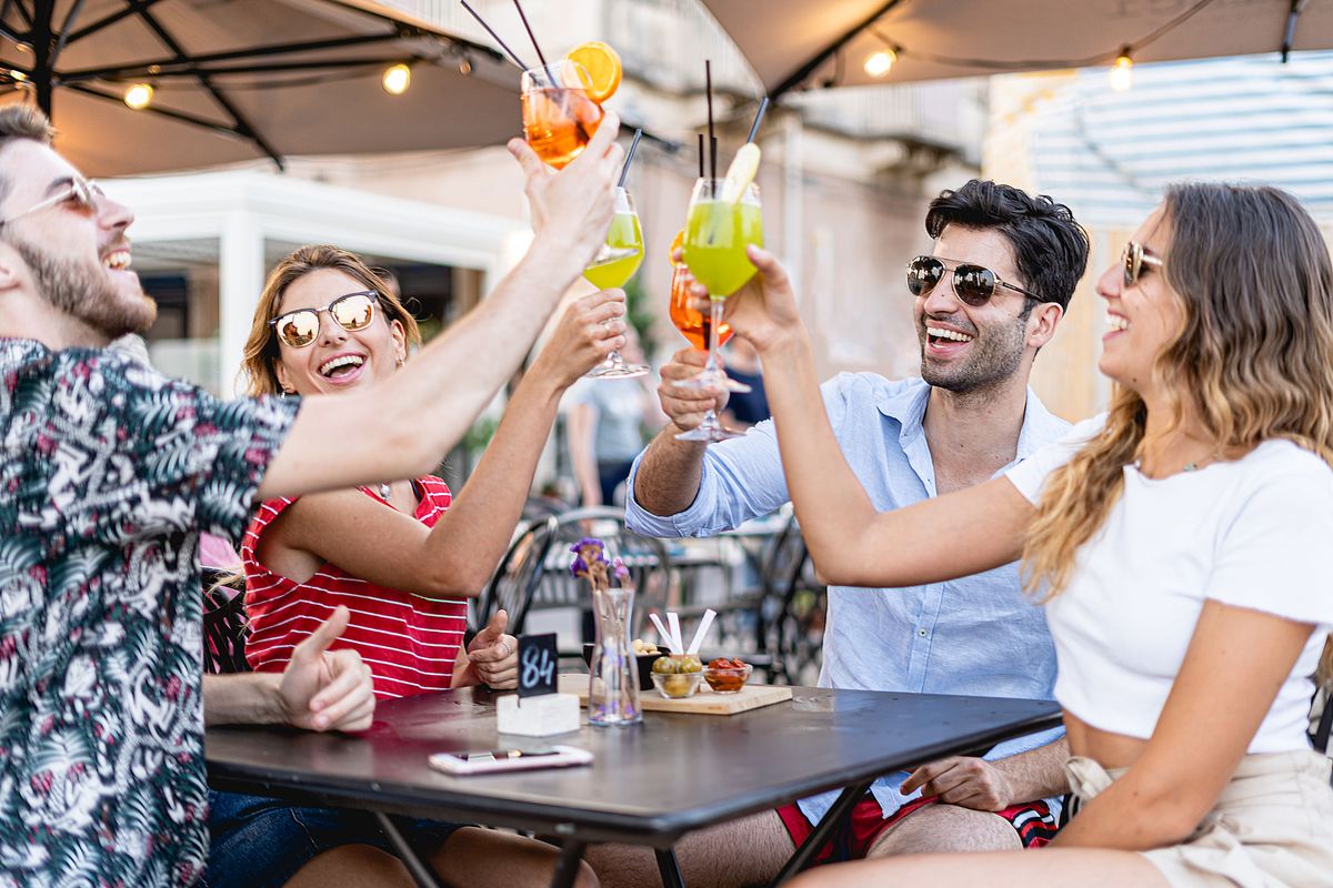 Four restaurant guests smile at the bar, drinks in their hands as they wait for their food table service.