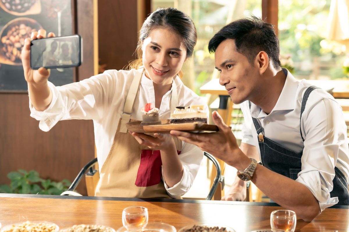 A new restaurant owner and restaurant chef pose for their social media marketing with their prepared food.