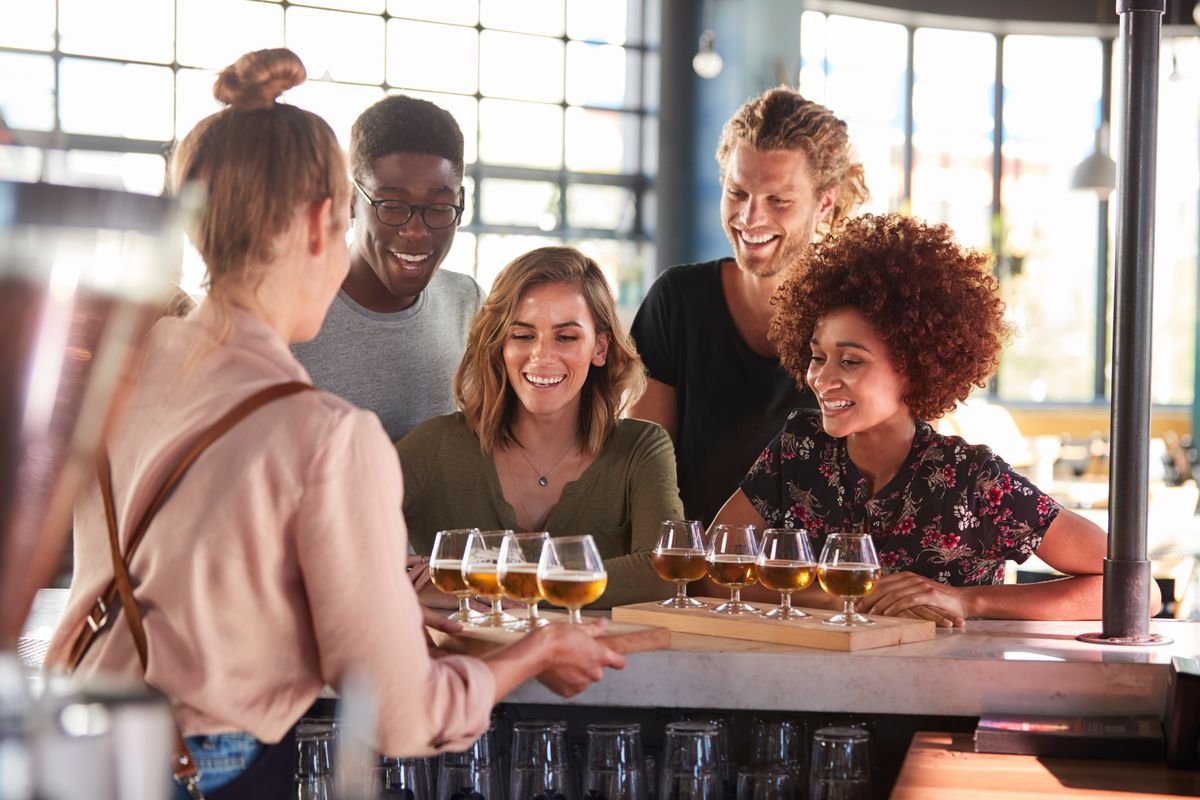 A group of people smile at a small brewery, being treated to two flights of beer.