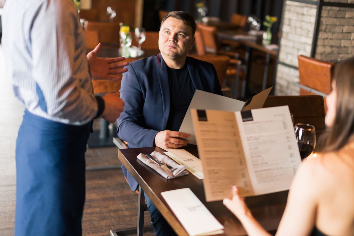 A waiter takes an order from a couple at a sit-down restaurant