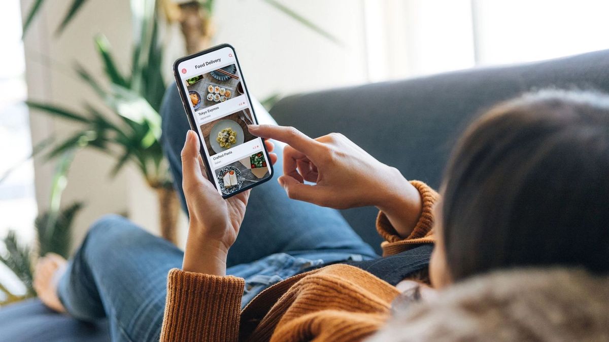 Woman lying on a sofa ordering food from her phone.