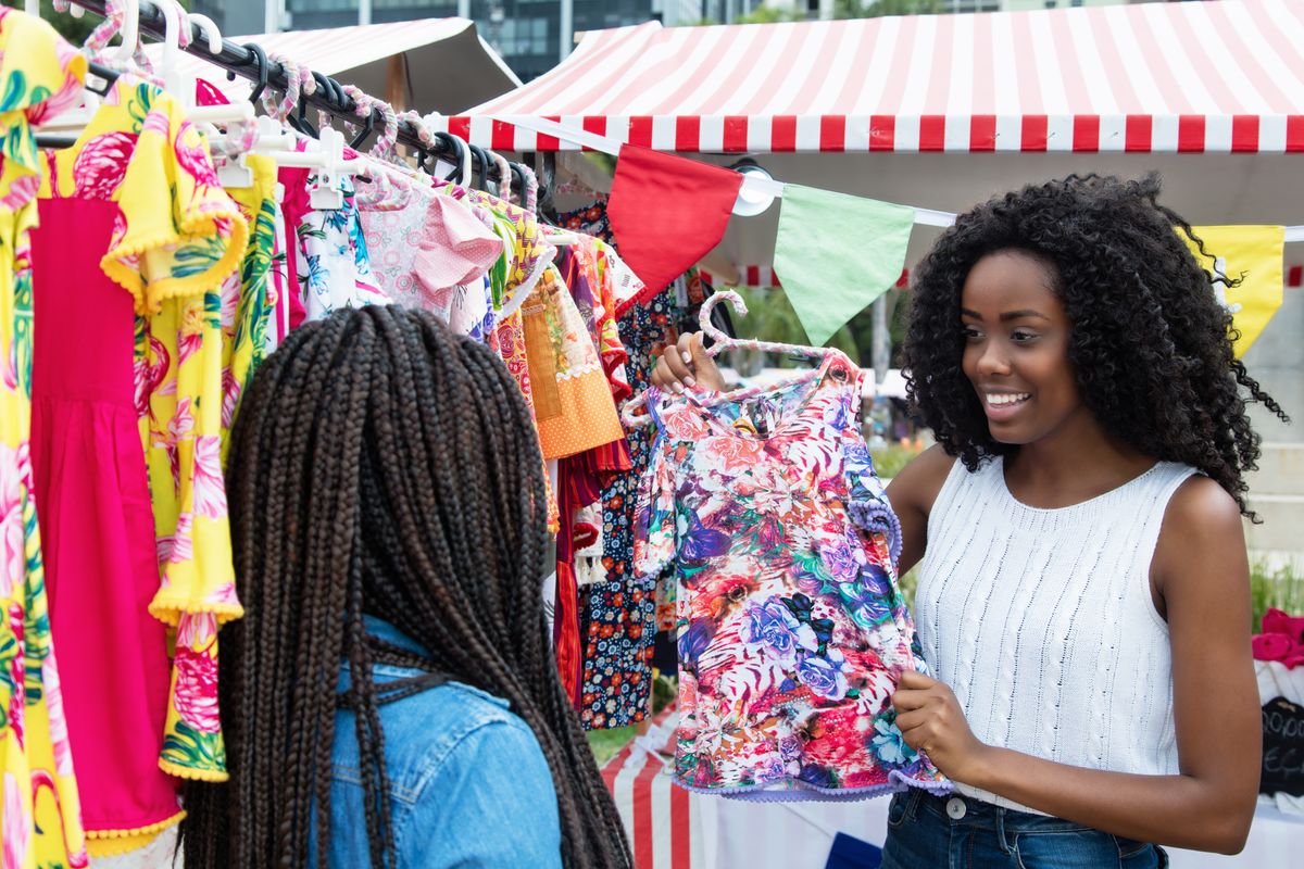 A small business owner shows a customer a blouse at a pop-up event for small businesses